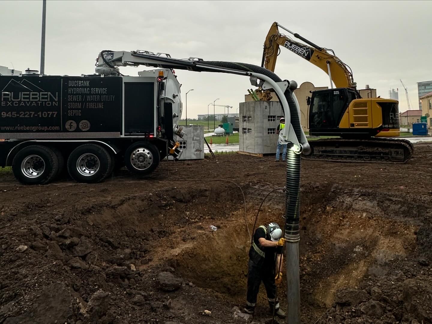 Rueben Excavation crew operating hydrovac wand exposing utilities in a deep excavation