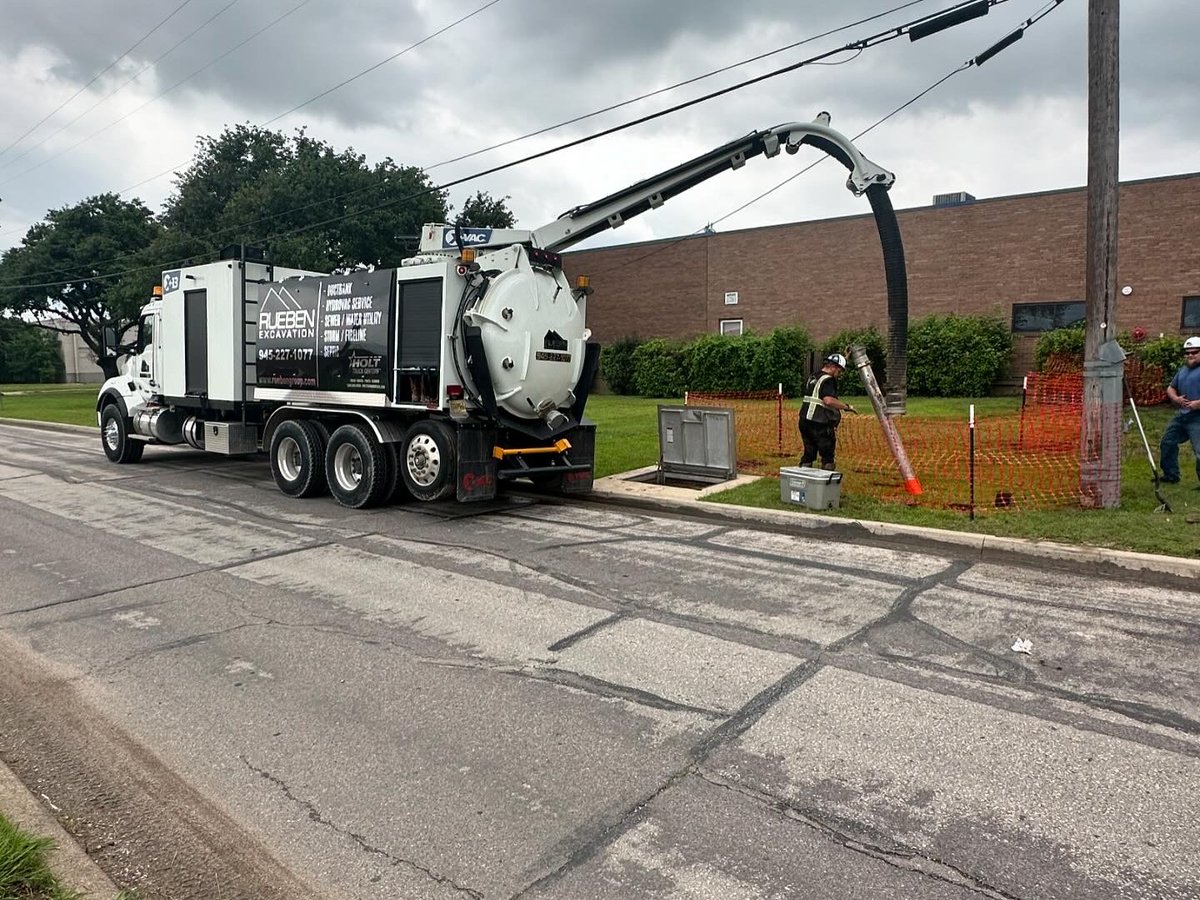 Rueben Excavation hydrovac truck daylighting utilities along a curb in a commercial corridor