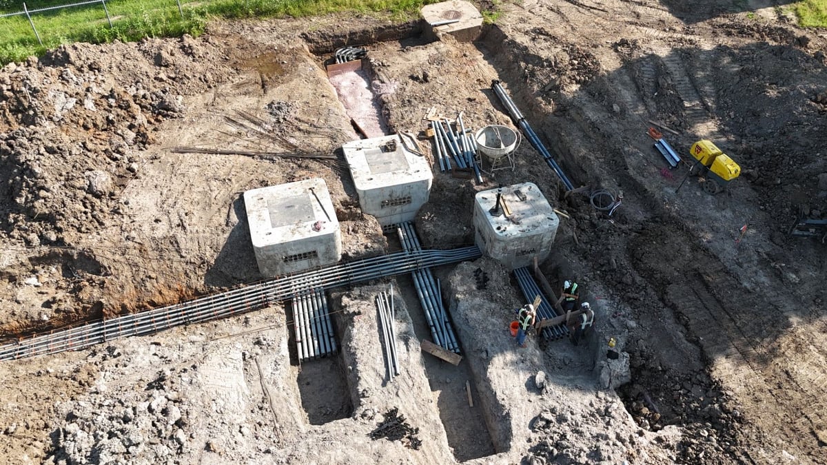 Aerial view of precast electrical vaults and PVC conduit runs being installed in an open duct bank excavation