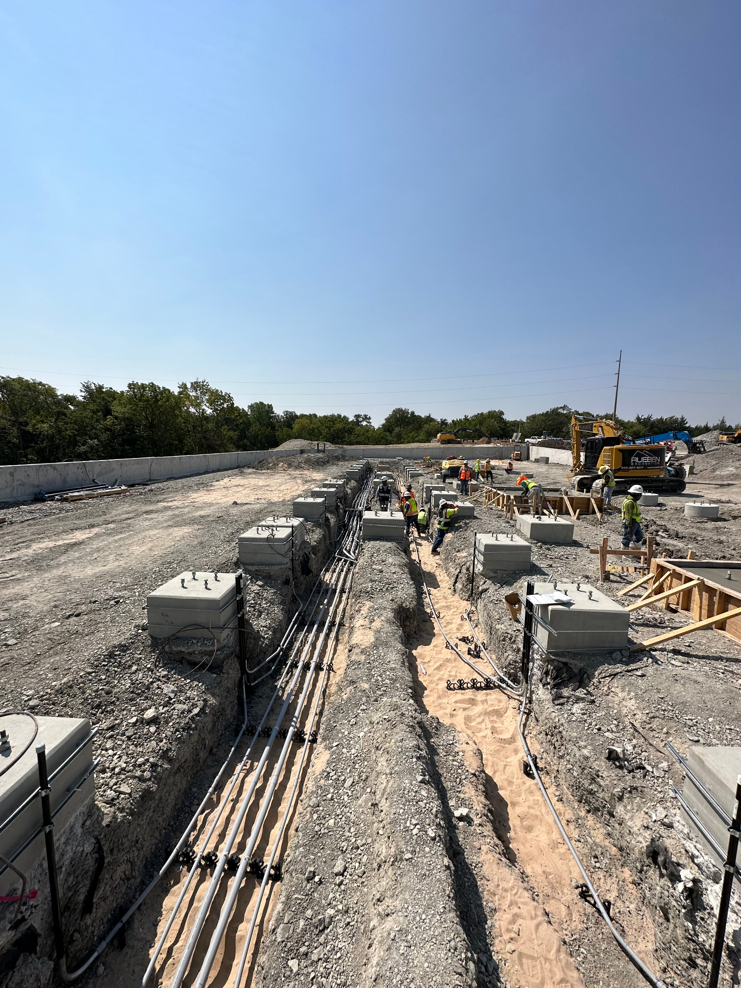 Row of concrete pull boxes along an open duct bank trench with Rueben Excavation crew working on a large utility corridor