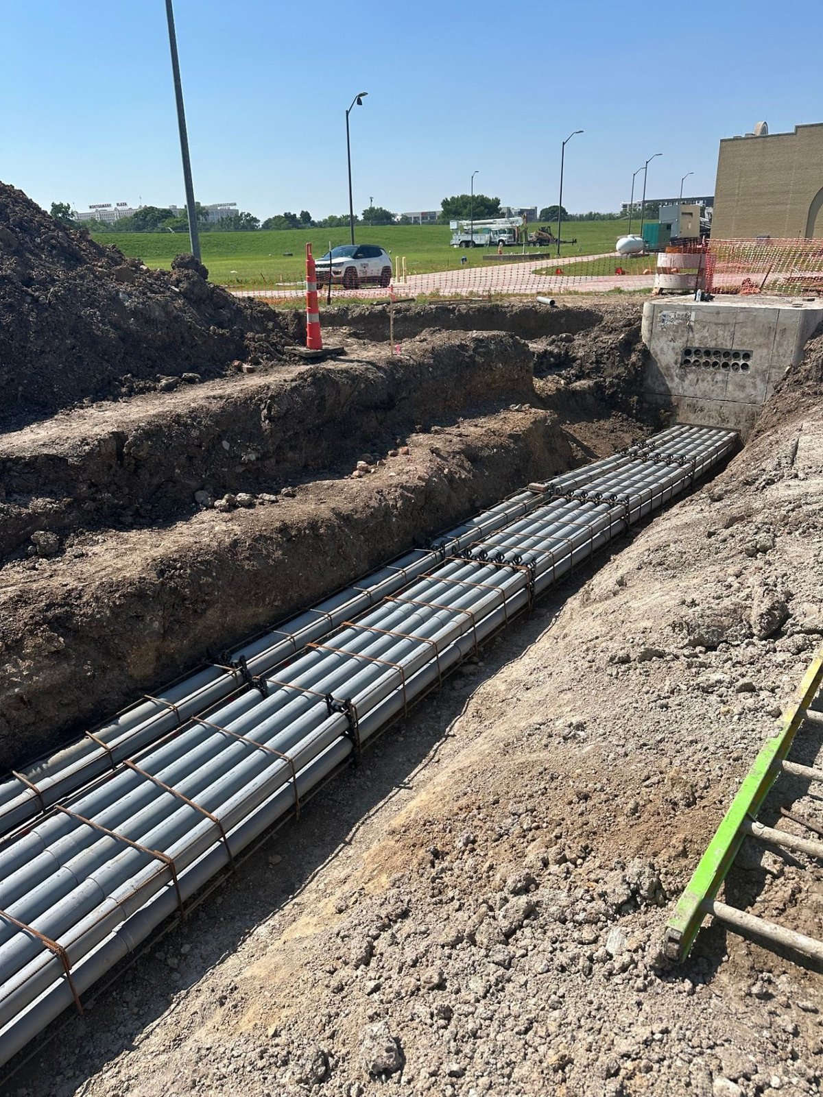 Long PVC conduit run secured in rebar cage inside an open duct bank trench next to a precast electrical vault