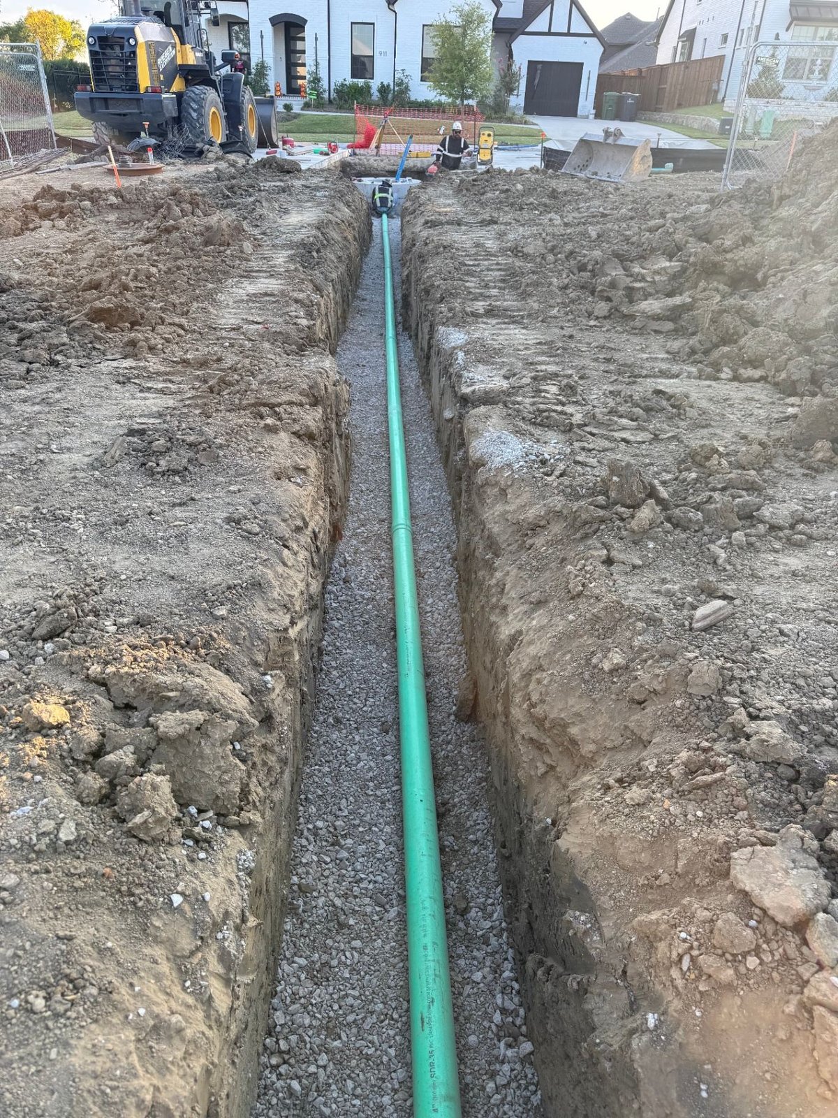 Green PVC sanitary sewer main laid on bedding stone in open trench at residential site