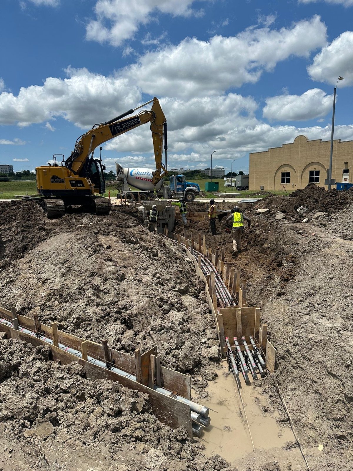 Rueben Excavation crew building concrete-encased duct bank formwork beside an excavator and concrete truck