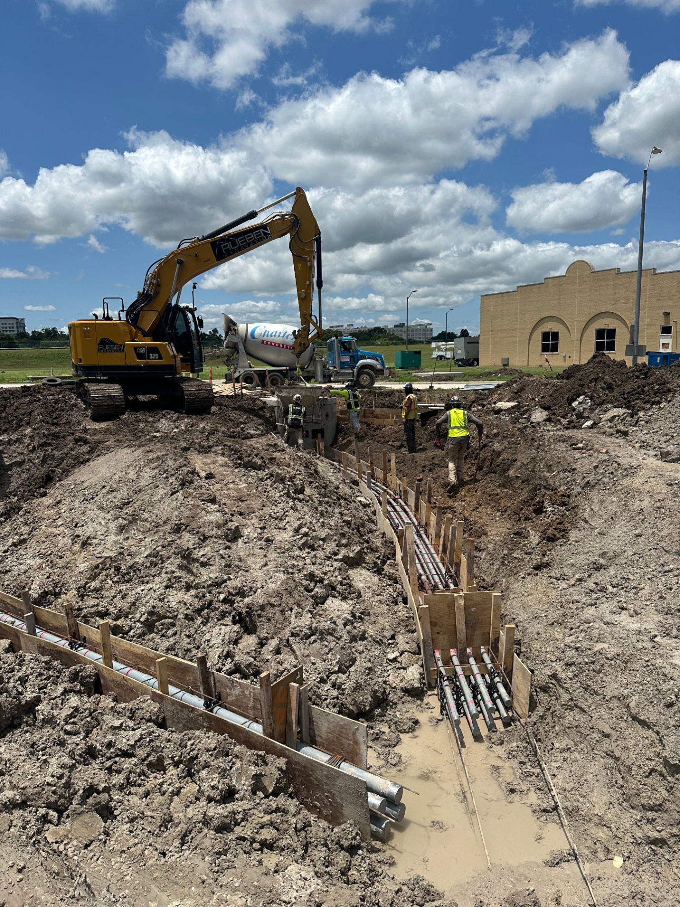 Rueben Excavation crew building concrete-encased duct bank formwork beside an excavator and concrete truck