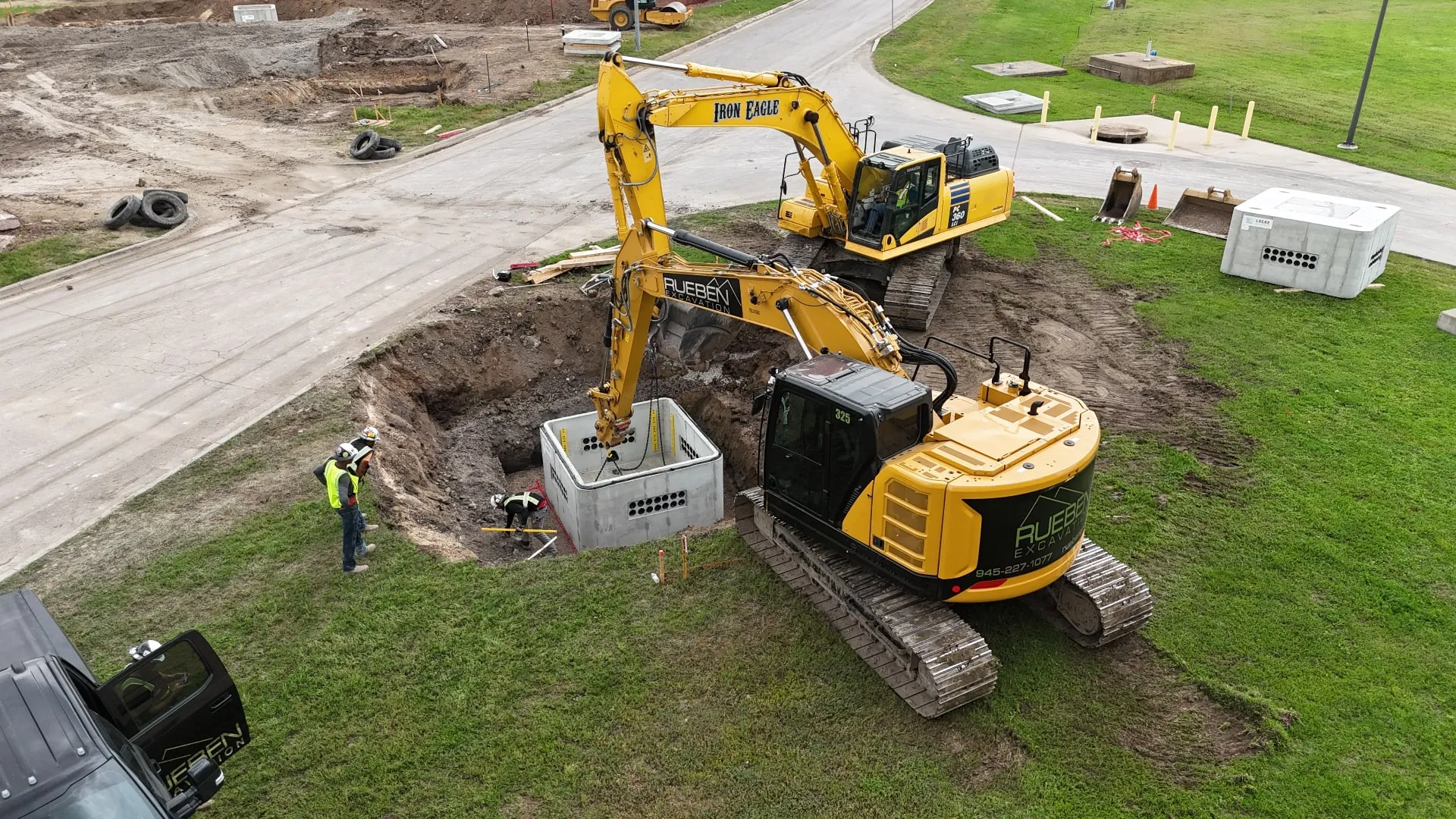 Aerial view of excavators setting a precast utility structure during duct bank construction